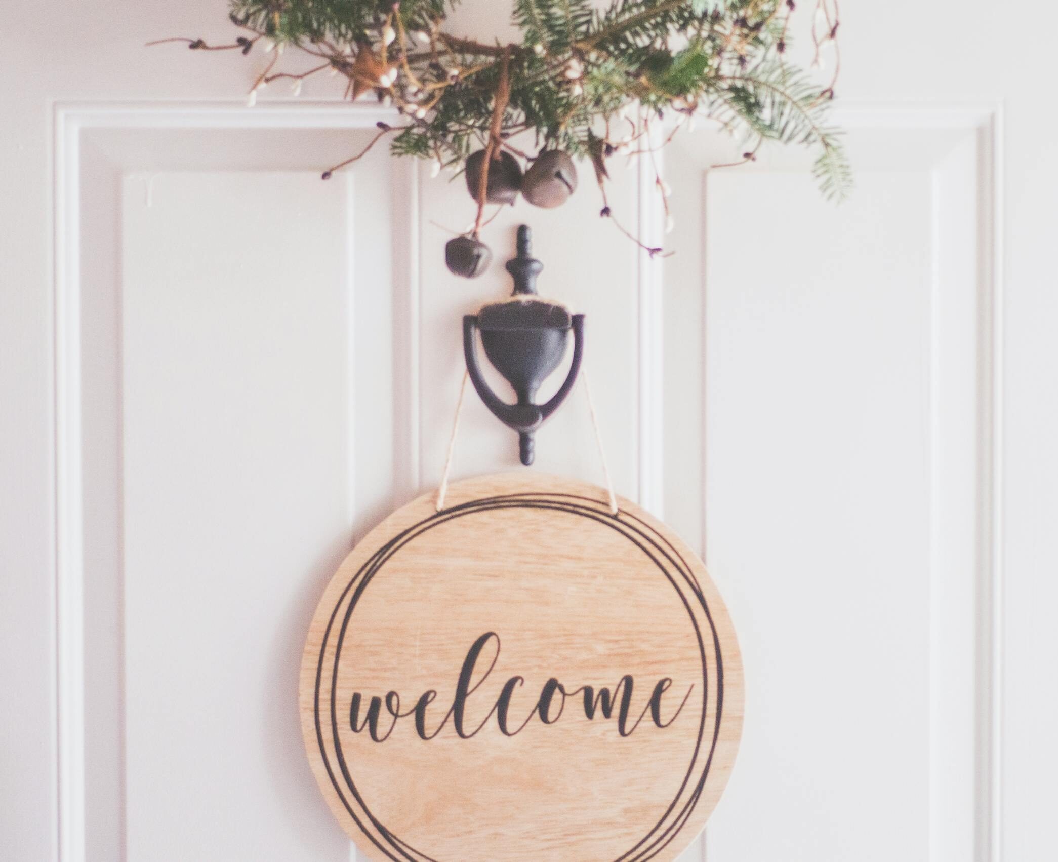 A stylish welcome sign with festive greenery on a door, perfect for home decoration.